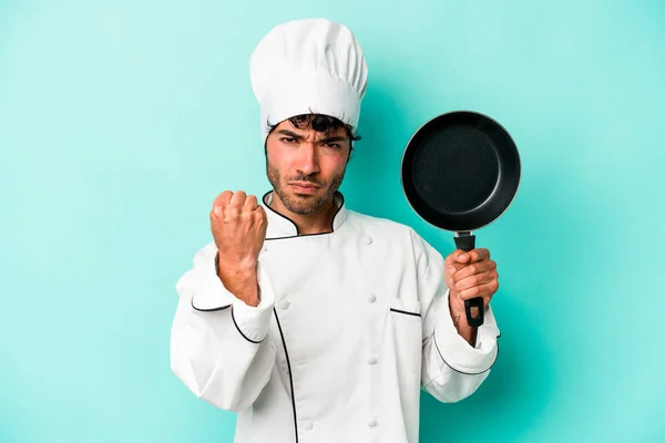年轻的高加索厨师手持飞盘 与蓝色背景隔离 对着相机显示拳头 咄咄逼人的面部表情 — 图库照片