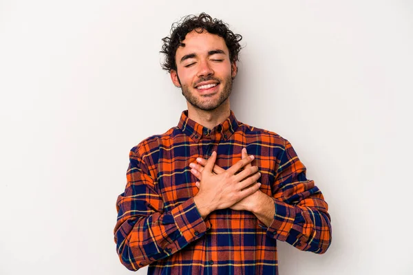 Beyaz arka planda soyutlanmış beyaz tenli genç bir adam gülüyor, elini yüreğine koyuyor, mutluluk kavramını koruyor..