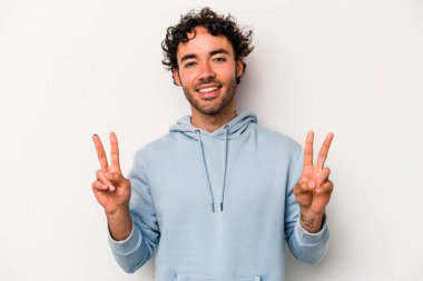 Beyaz arka planda izole edilmiş genç beyaz bir adam zafer işareti gösteriyor ve gülümsüyor..