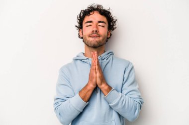Beyaz arka planda izole edilmiş genç beyaz bir adam el ele tutuşup, ağız kenarında dua ediyor, kendinden emin..