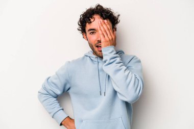 Beyaz arka planda izole edilmiş genç beyaz bir adam yüzünün yarısını palmiye ile örterek eğleniyor..