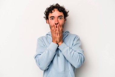 Beyaz arka planda izole edilmiş genç beyaz adam elleriyle ağzını kapatırken şok oldu..