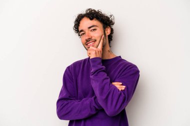 Beyaz arka planda izole olmuş genç beyaz bir adam gülümsüyor ve kendinden emin, çenesine elleriyle dokunuyor..