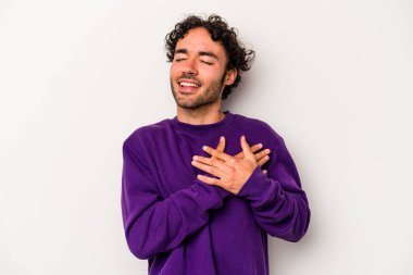 Beyaz arka planda soyutlanmış beyaz tenli genç bir adam gülüyor, elini yüreğine koyuyor, mutluluk kavramını koruyor..