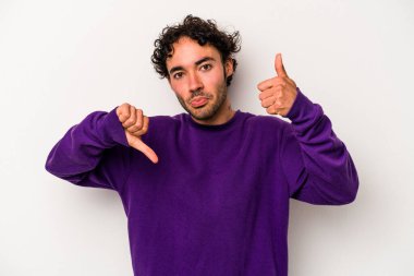 Beyaz arka planda izole edilmiş genç beyaz bir adam baş parmaklarını aşağı ve yukarı kaldırıyor, zor seçim konsepti