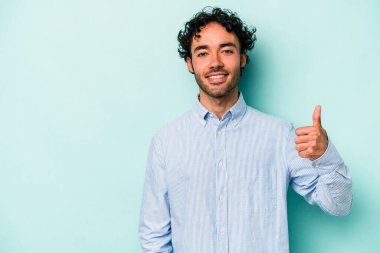 Beyaz arka planda izole edilmiş genç beyaz adam gülümsüyor ve başparmağını kaldırıyor.