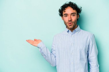 Beyaz arka planda izole edilmiş genç beyaz adam, avuç içi fotokopi alanını elinde tutmaktan etkilenmiş..