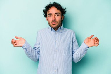 Beyaz arka planda izole edilmiş genç beyaz bir adam sorgulama sırasında omuz silkiyor ve şüphe duyuyor..