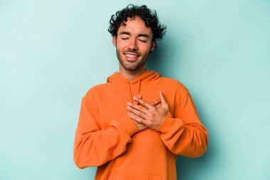 Beyaz arka planda soyutlanmış beyaz tenli genç bir adam gülüyor, elini yüreğine koyuyor, mutluluk kavramını koruyor..