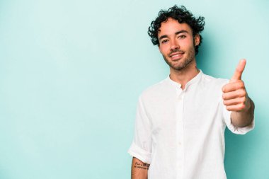 Beyaz arka planda izole edilmiş genç beyaz adam gülümsüyor ve başparmağını kaldırıyor.