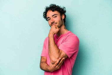 Beyaz arka planda izole olmuş genç beyaz bir adam gülümsüyor ve kendinden emin, çenesine elleriyle dokunuyor..