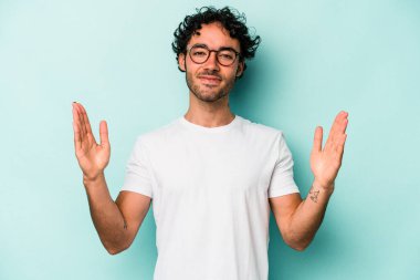 Beyaz arka planda izole edilmiş genç beyaz bir adam işaret parmaklarıyla küçük bir şey tutuyor, gülümsüyor ve kendinden emin..