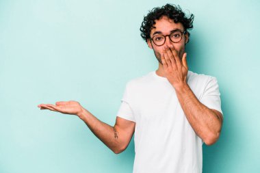 Beyaz arka planda izole edilmiş genç beyaz adam, avuç içi fotokopi alanını elinde tutmaktan etkilenmiş..