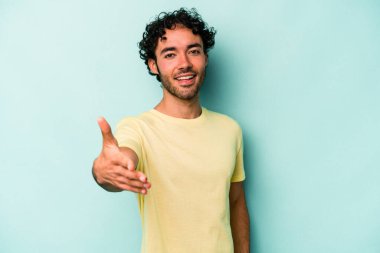 Beyaz arka planda izole edilmiş genç beyaz bir adam selamlama jesti olarak kameraya elini uzatıyor..