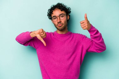 Beyaz arka planda izole edilmiş genç beyaz bir adam baş parmaklarını aşağı ve yukarı kaldırıyor, zor seçim konsepti