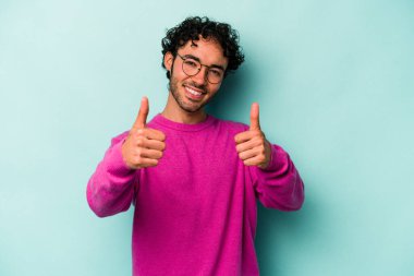 Beyaz arka planda izole edilmiş genç beyaz bir adam iki parmağını da kaldırıyor, gülümsüyor ve kendinden emin..