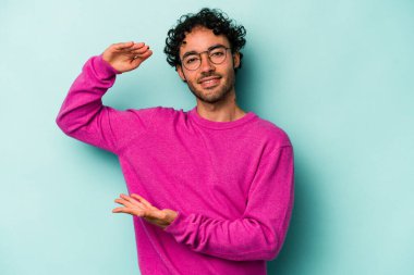 Beyaz arka planda izole edilmiş genç beyaz bir adam işaret parmaklarıyla küçük bir şey tutuyor, gülümsüyor ve kendinden emin..