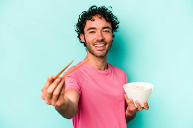 Mavi arka planda izole edilmiş erişte yiyen genç beyaz bir adam.