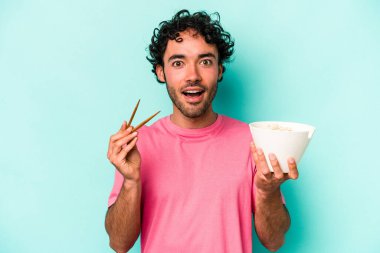 Mavi arka planda izole edilmiş erişte yiyen genç beyaz bir adam.