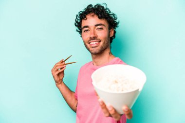 Mavi arka planda izole edilmiş erişte yiyen genç beyaz bir adam.