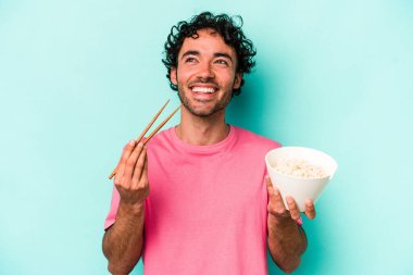 Mavi arka planda izole edilmiş erişte yiyen genç beyaz bir adam.