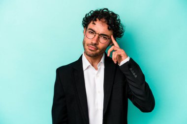 Kafkasyalı genç iş adamı, mavi arka planda izole edilmiş, parmağıyla tapınağı işaret eden, düşünen, bir göreve odaklanmış..