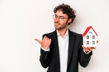 Beyaz arka plan noktalarından izole edilmiş beyaz bir oyuncak evi tutan Kafkasyalı genç bir iş adamı başparmak uzakta, gülüyor ve kaygısız.