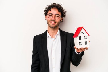 Beyaz arka planda izole edilmiş bir oyuncak evi tutan Kafkasyalı genç bir iş adamı mutlu, güler yüzlü ve neşeli..