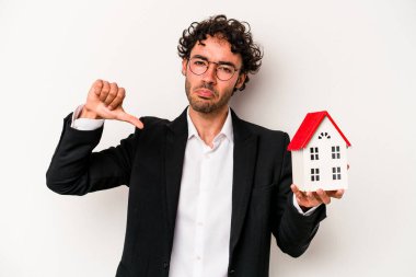 Beyaz arka planda izole edilmiş bir oyuncak evi tutan Kafkasyalı genç iş adamı gururlu ve kendinden emin hissediyor, örnek olarak..