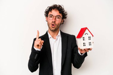 Beyaz arka planda izole edilmiş bir oyuncak evi tutan Kafkasyalı genç bir iş adamı harika bir fikre sahip, yaratıcılık kavramı..