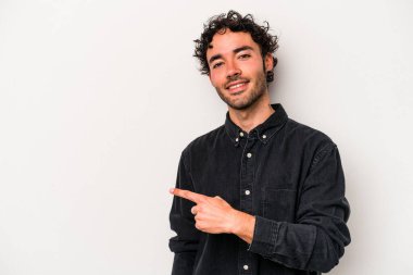 Beyaz arka planda izole edilmiş genç beyaz bir adam gülümsüyor ve boş alanda bir şeyler gösteriyor..