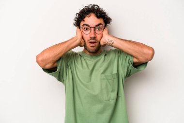 Beyaz arka planda izole edilmiş genç beyaz bir adam kulakları kulaklarıyla kapatıyor ve çok ses duymamaya çalışıyor..