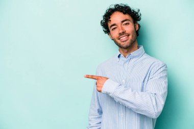 Beyaz arka planda izole edilmiş genç beyaz bir adam gülümsüyor ve boş alanda bir şeyler gösteriyor..