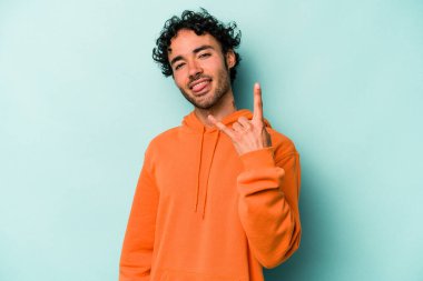 Beyaz arka planda izole edilmiş genç beyaz bir adam parmaklarıyla kaya hareketi gösteriyor.