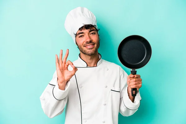 年轻的高加索厨师 拿着一只被蓝色背景隔离的飞盘 快乐而自信地做出了好的姿态 — 图库照片