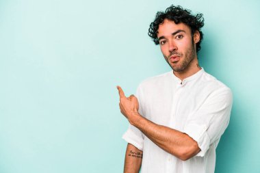 Beyaz arka planda izole edilmiş genç beyaz bir adam gülümsüyor ve boş alanda bir şeyler gösteriyor..