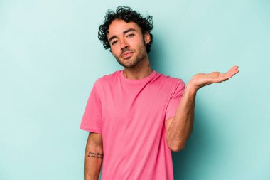 Beyaz arka planda izole edilmiş genç beyaz bir adam sorgulama sırasında omuz silkiyor ve şüphe duyuyor..