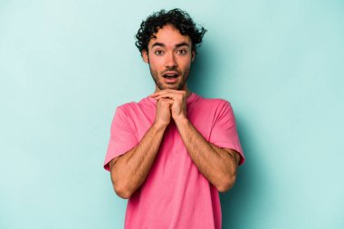 Beyaz arka planda izole edilmiş genç beyaz bir adam şans için dua ediyor, şaşırmış ve ağzını açıp önüne bakıyor..