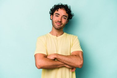 Beyaz arka planda kendini güvende hisseden, kararlılıkla kollarını kavuşturan beyaz tenli genç bir adam..