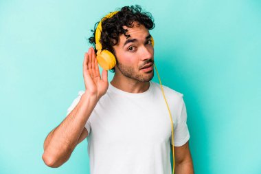 Mavi arka planda izole edilmiş müzik dinleyen beyaz bir adam bir dedikoduyu dinlemeye çalışıyor..