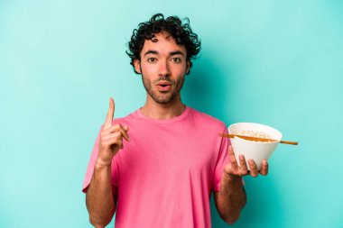 Mavi arka planda izole edilmiş erişte yiyen genç beyaz adam, yaratıcılık kavramı hakkında harika bir fikre sahip..