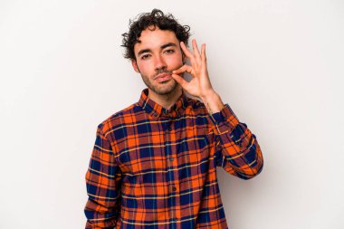 Beyaz arka planda izole edilmiş beyaz tenli genç bir adam parmakları dudaklarında bir sır saklıyor..