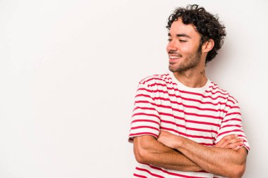 Beyaz arka planda izole edilmiş genç beyaz adam kollarını kavuşturarak gülümsüyor..