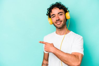 Mavi arka planda izole edilmiş müzik dinleyen beyaz bir adam gülümsüyor ve boş alanda bir şeyler gösteriyor..