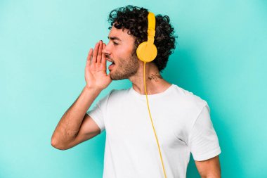 Mavi arka planda izole edilmiş müzik dinleyen genç beyaz adam bağırıyor ve avuç içini açık tutuyor..