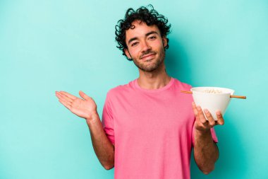 Mavi arka planda izole edilmiş erişte yiyen genç beyaz adam bir palmiye üzerinde fotokopi alanı ve belinde başka bir el tutuyor..