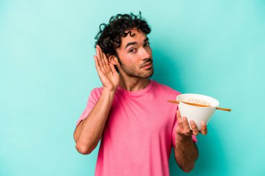 Mavi arka planda izole edilmiş erişte yiyen genç beyaz adam bir dedikoduyu dinlemeye çalışıyor..