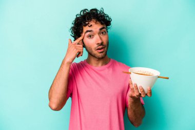 Mavi arka planda izole edilmiş erişte yiyen genç beyaz adam işaret parmağıyla yaptığı hayal kırıklığını gösteriyor..
