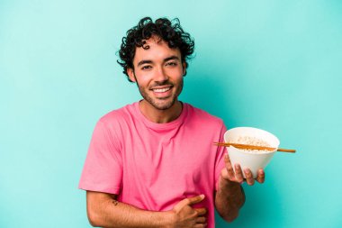 Mavi arka planda izole edilmiş erişte yiyen genç beyaz adam gülüyor ve eğleniyor..