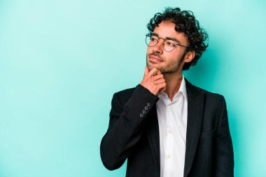 Kafkasyalı genç iş adamı mavi arka planda izole edilmiş şüpheli ve şüpheci bir ifadeyle yana bakıyor..